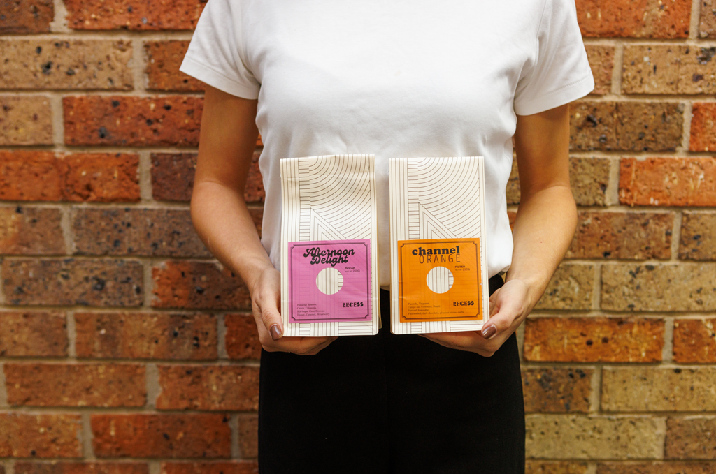 Close up of a person holding two bags of coffee beans in front of a brick wall